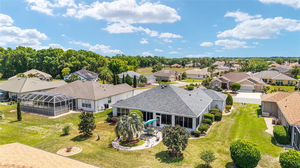 An aerial view shows suburban houses with screened-in lanais and landscaped backyards under a blue sky — 9290 SE 120TH LOOP, SUMMERFIELD, FL