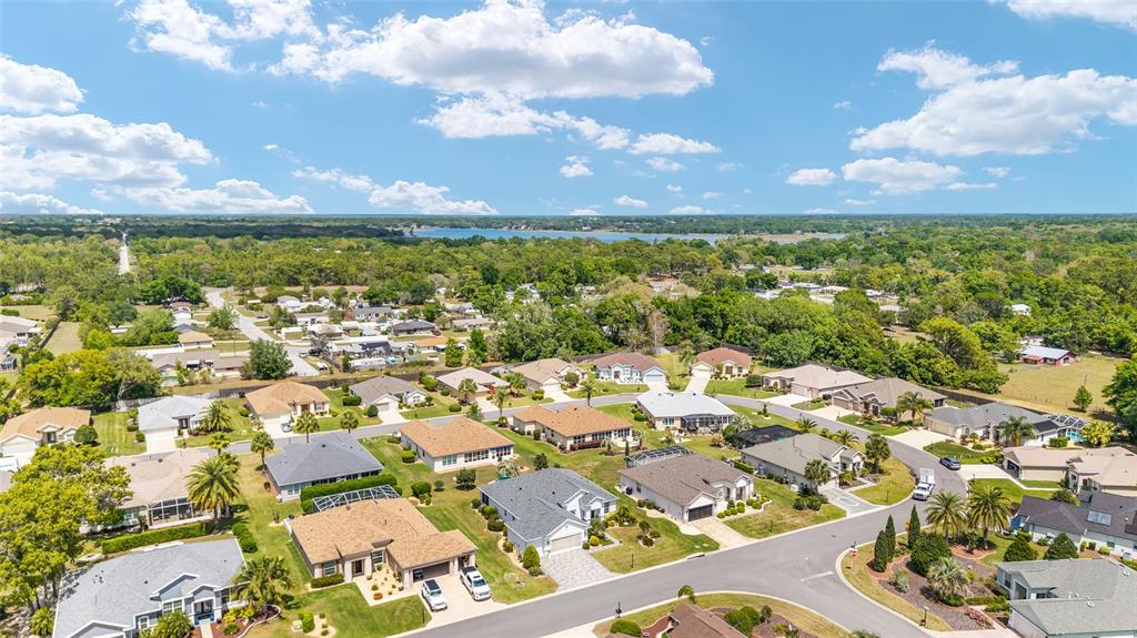 An aerial view of a suburban neighborhood with single-family homes, trees, and a distant lake — 9290 SE 120TH LOOP, SUMMERFIELD, FL