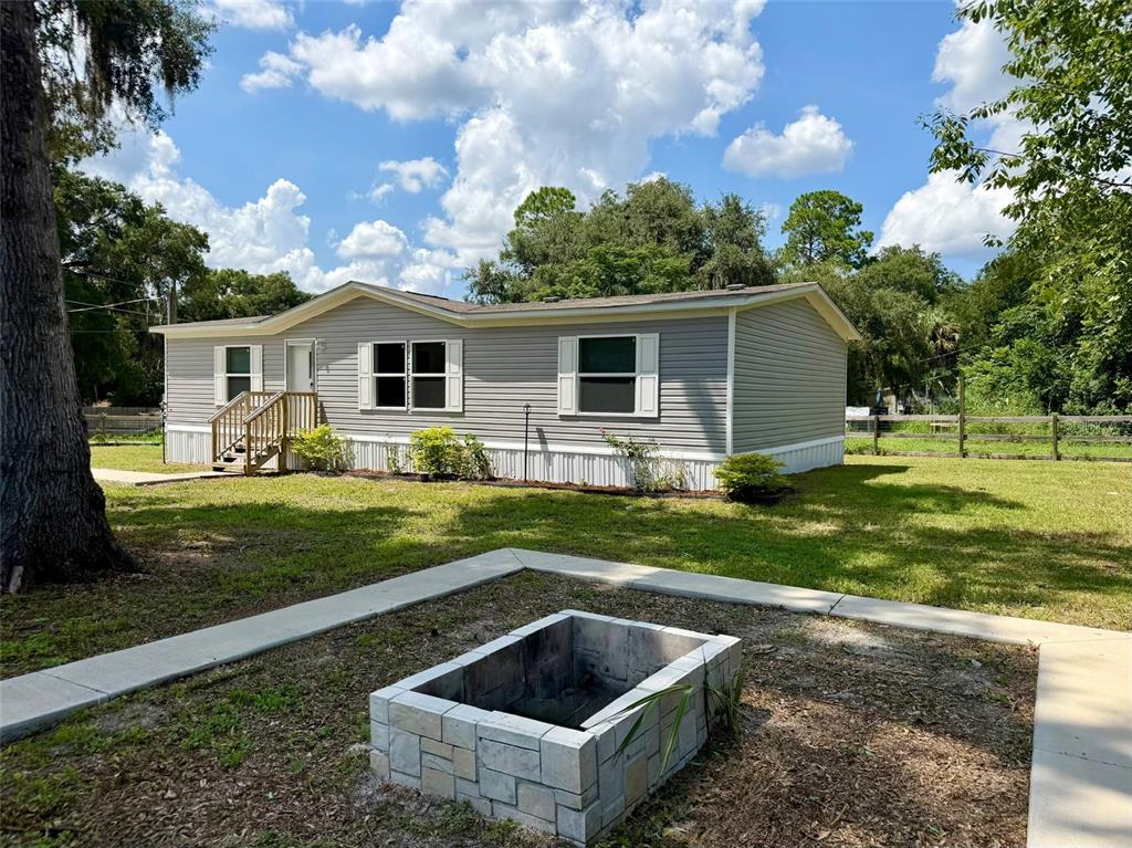 A gray manufactured home sits on a grassy lot with a stone fire pit nearby — 11057 SE 132ND PLACE, OCKLAWAHA, FL