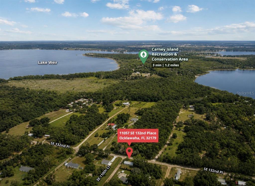 An aerial view shows a house surrounded by trees near a large lake — 11057 SE 132ND PLACE, OCKLAWAHA, FL