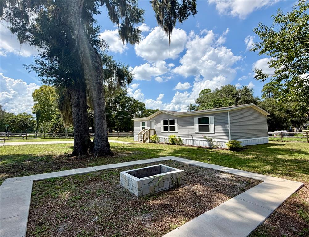 A light gray manufactured home sits on a grassy lot with a stone fire pit — 11057 SE 132ND PLACE, OCKLAWAHA, FL