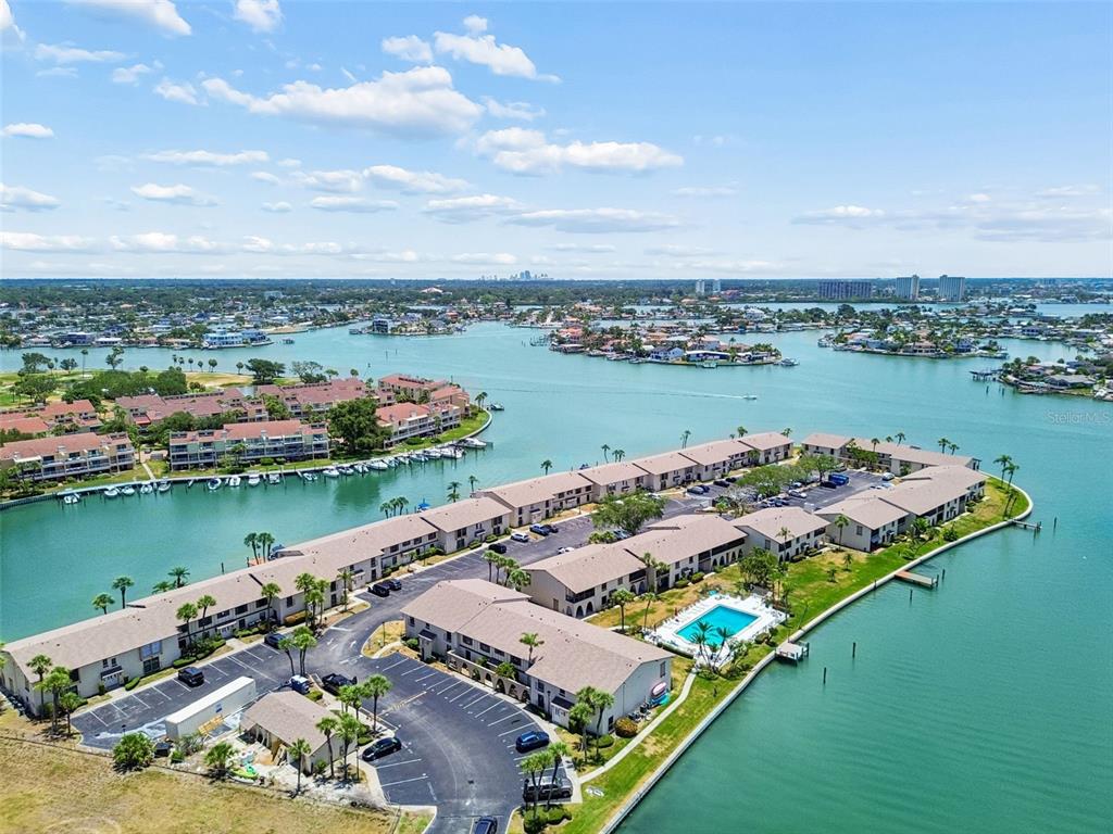 An aerial view shows a waterfront condominium complex with a swimming pool and parking lot — 505 PLAZA SEVILLE COURT UNIT 12, TREASURE ISLAND, FL