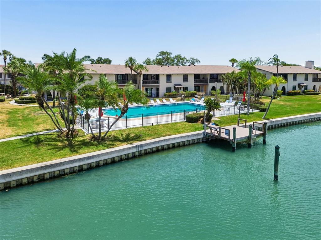 An outdoor swimming pool sits beside a canal with a small wooden boat dock — 505 PLAZA SEVILLE COURT UNIT 12, TREASURE ISLAND, FL