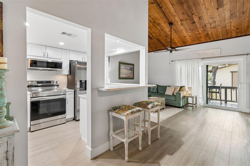A kitchen with white cabinets and stainless steel appliances opens to a living room area — 505 PLAZA SEVILLE COURT UNIT 12, TREASURE ISLAND, FL