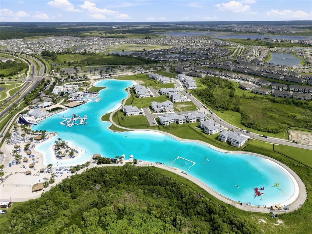 An aerial view of a large turquoise lagoon surrounded by residential buildings and green space — 7697 ROMA DUNE DRIVE, WESLEY CHAPEL, FL