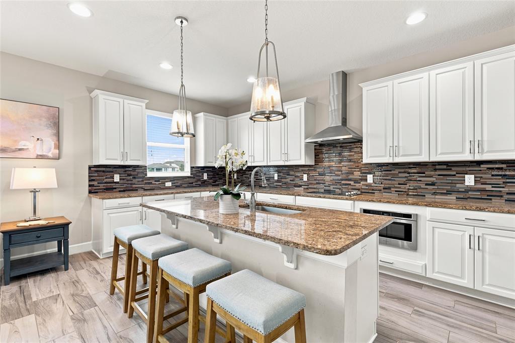 A kitchen with white cabinets, granite countertops, a center island with stools, and tile flooring — 7697 ROMA DUNE DRIVE, WESLEY CHAPEL, FL