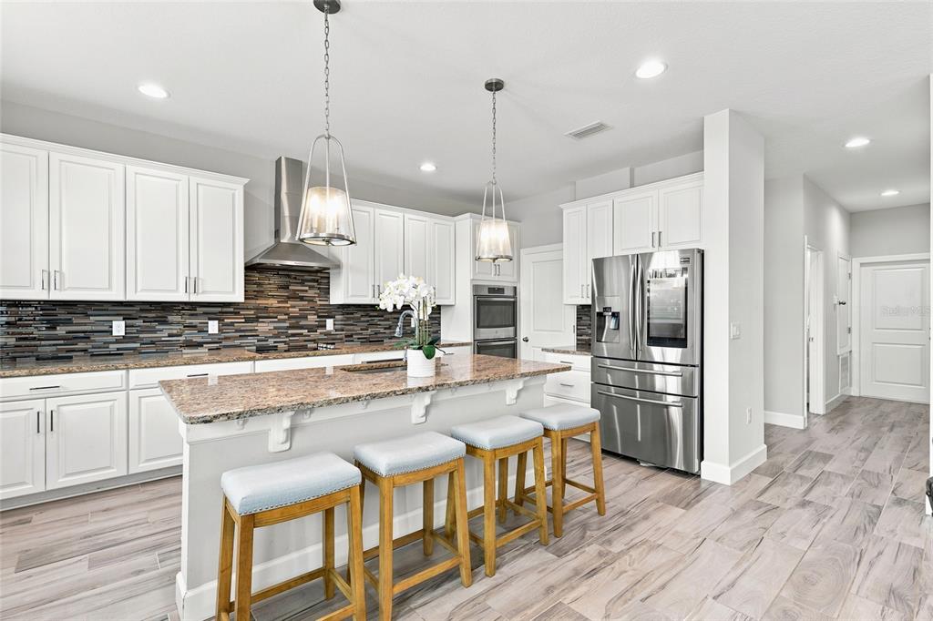 A modern kitchen features white cabinets, granite countertops, a tiled backsplash, and a center island — 7697 ROMA DUNE DRIVE, WESLEY CHAPEL, FL