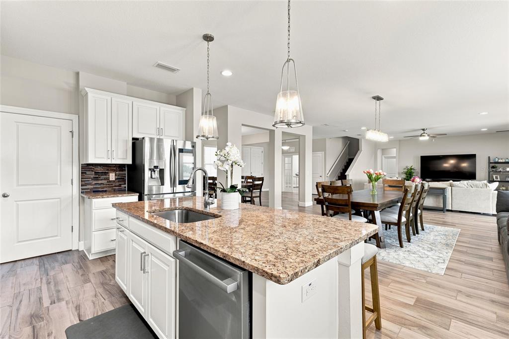 A kitchen with granite countertops and white cabinets overlooks an open-concept dining and living area — 7697 ROMA DUNE DRIVE, WESLEY CHAPEL, FL