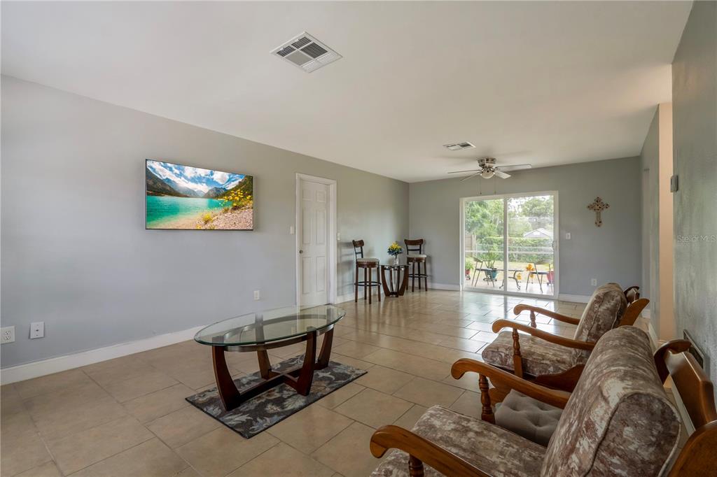 A living room with tile floors, a glass coffee table, and sliding glass patio doors — 2633 BEAL STREET, DELTONA, FL