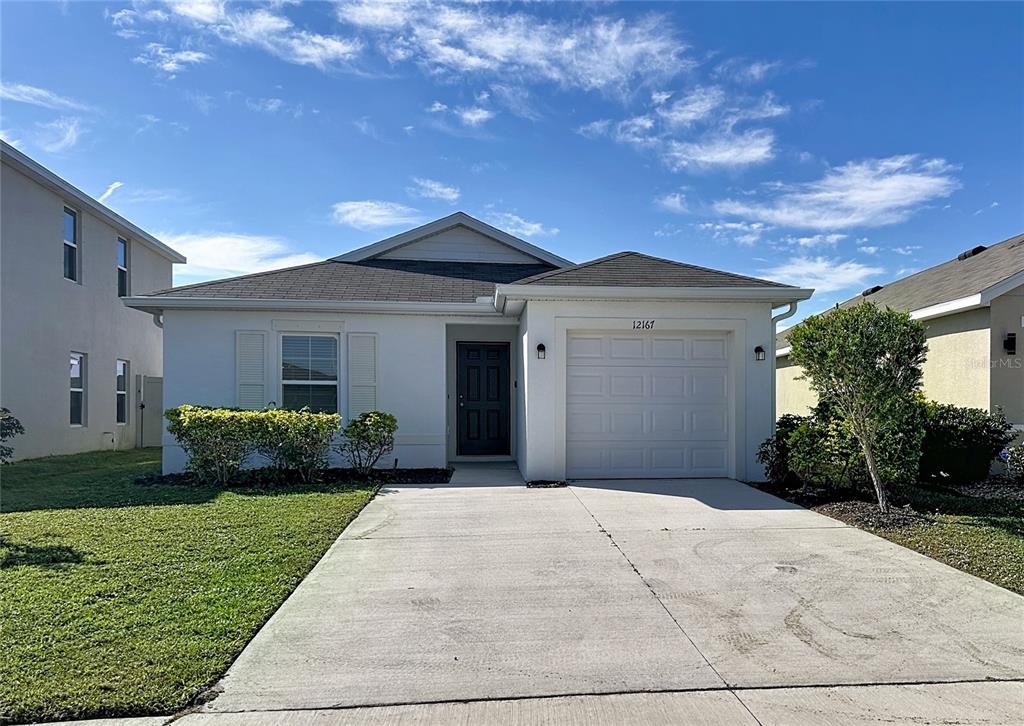 A single-story white house features a front-facing garage, a dark door, and a concrete driveway — 12167 HIGH ROCK WAY, PARRISH, FL
