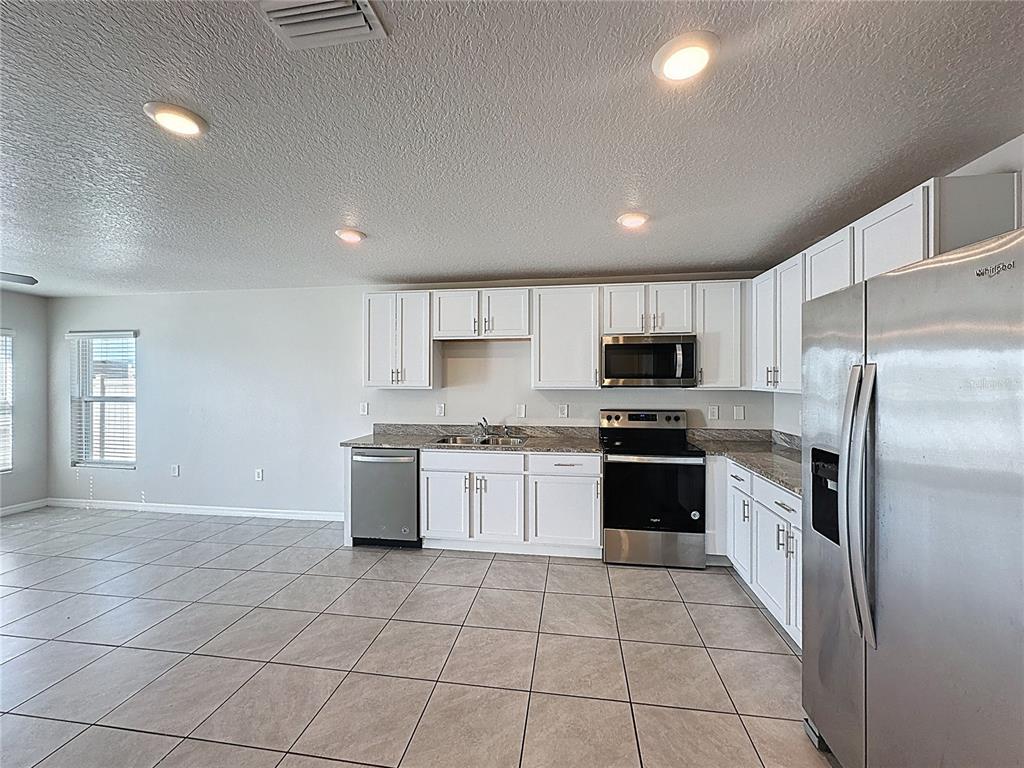 A kitchen features white cabinets, stainless steel appliances, and light-colored tile flooring — 12167 HIGH ROCK WAY, PARRISH, FL