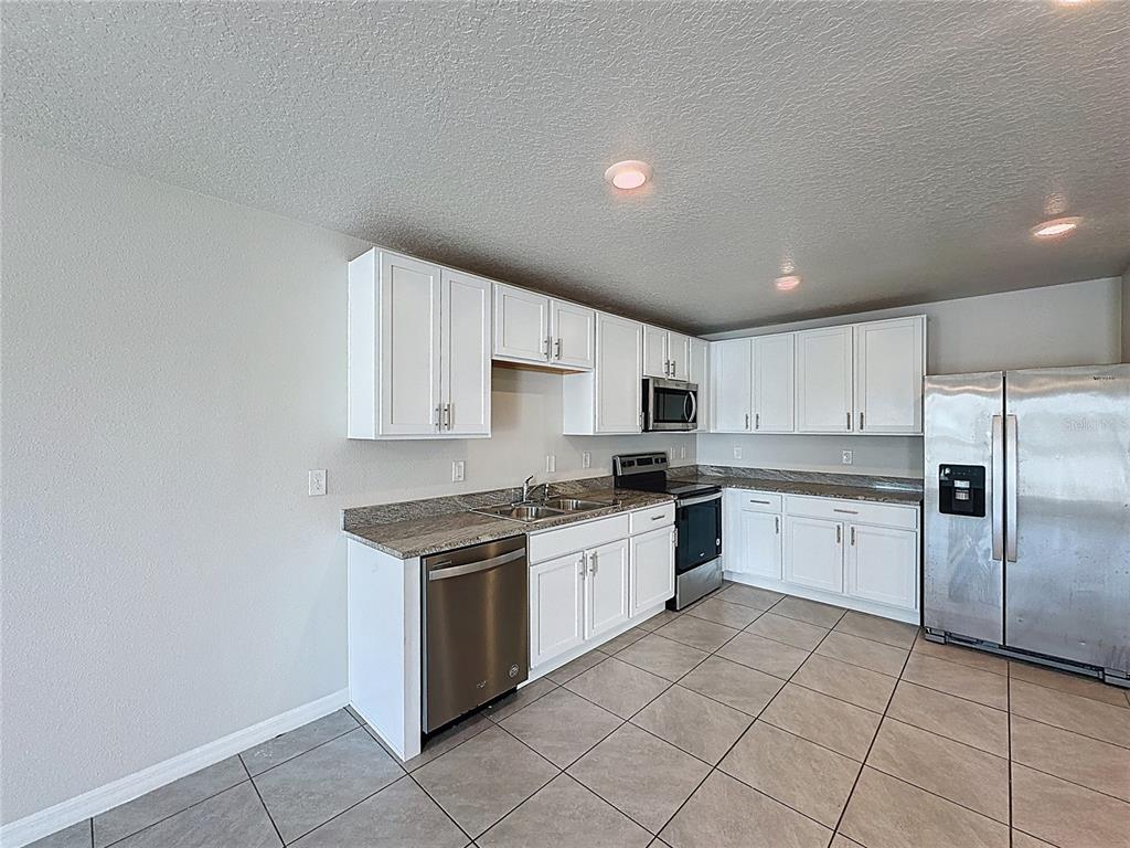 A kitchen features white cabinets, stainless steel appliances, granite countertops, and light-colored tile flooring — 12167 HIGH ROCK WAY, PARRISH, FL