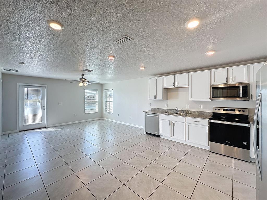 A kitchen with white cabinets and stainless steel appliances opens into a tiled living area — 12167 HIGH ROCK WAY, PARRISH, FL