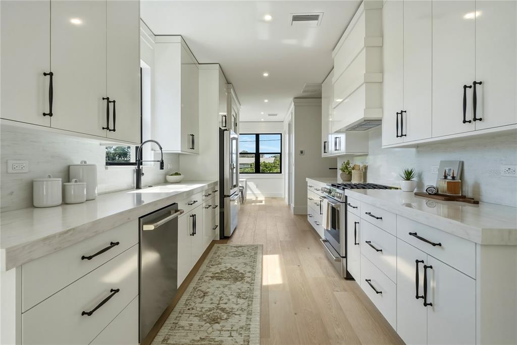 A galley kitchen features white cabinets, quartz countertops, stainless steel appliances, and light wood flooring — 205 BATES AVENUE UNIT A, INDIAN ROCKS BEACH, FL