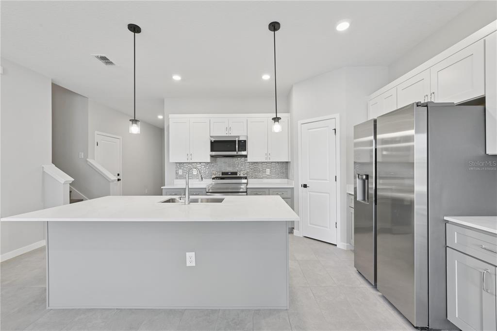 A modern kitchen features a large white island, stainless steel appliances, and white cabinetry — 17843 SW 68TH PLACE, DUNNELLON, FL