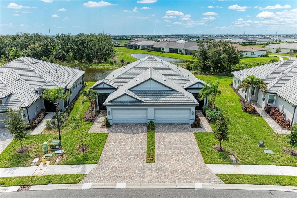 An aerial view shows a duplex home with a paver driveway and a tiled roof — 18048 CHERISHED LOOP, LAKEWOOD RANCH, FL