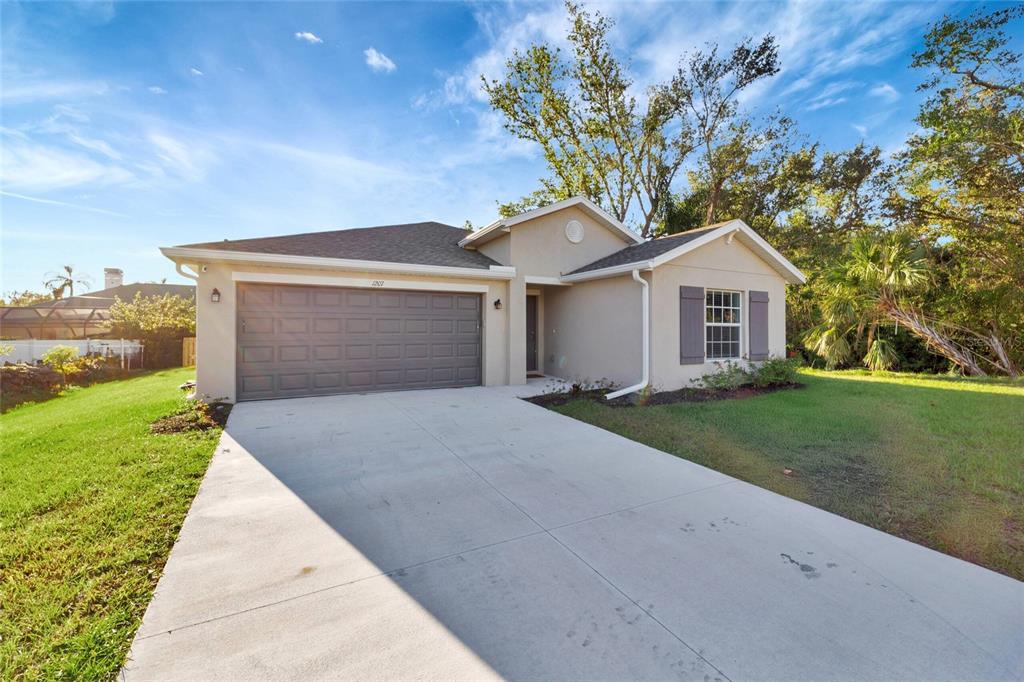 A single-story house with a beige stucco exterior, a gray garage door, and a concrete driveway — 1207 SHEEHAN BOULEVARD, PORT CHARLOTTE, FL