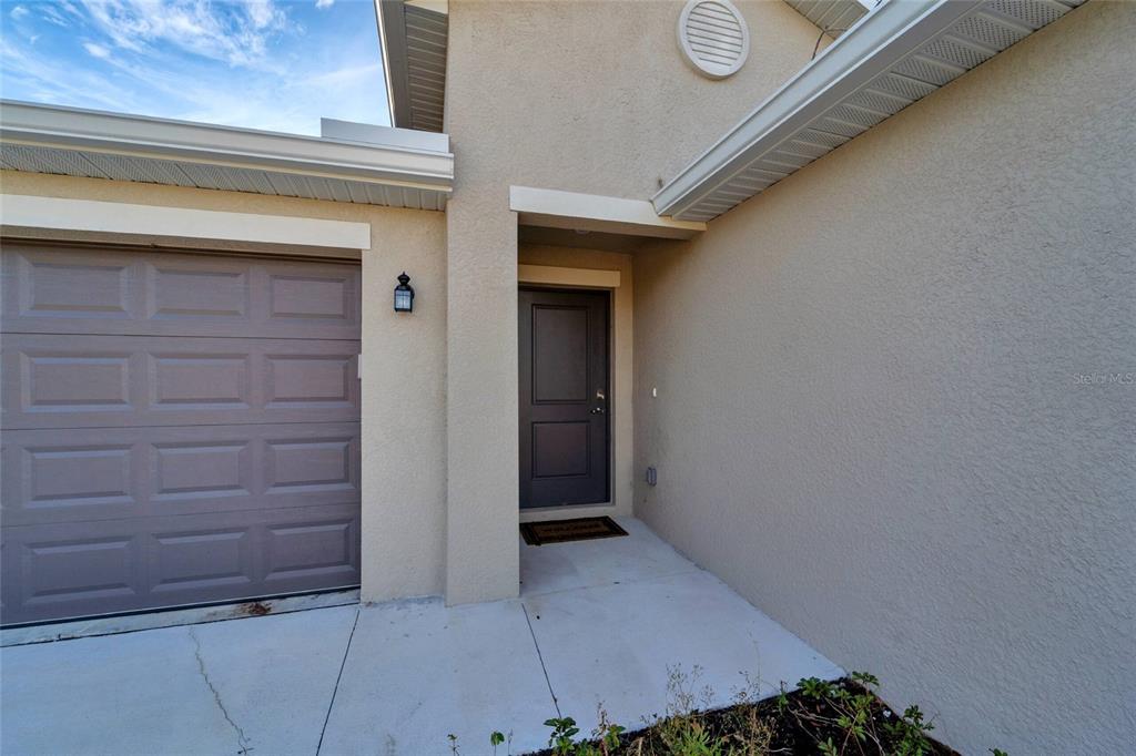 A beige stucco house exterior features a dark front door and a gray garage door — 1207 SHEEHAN BOULEVARD, PORT CHARLOTTE, FL