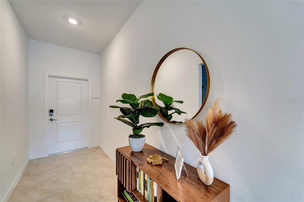 A bright entryway features a wooden console table, a round gold mirror, and a potted plant — 1207 SHEEHAN BOULEVARD, PORT CHARLOTTE, FL