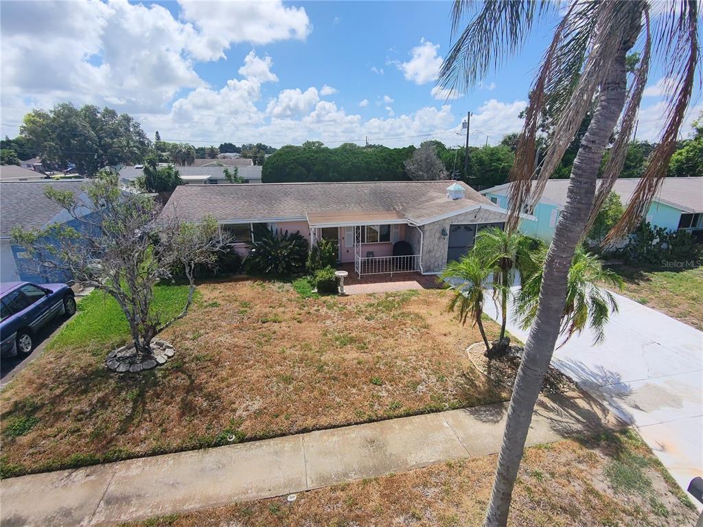 An elevated view of a single-story house with a pink exterior, stone accents, and driveway — 1248 ERMINE DRIVE, HOLIDAY, FL