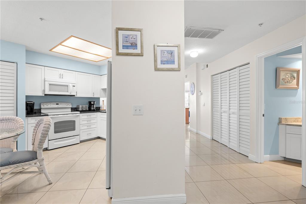 A kitchen with white cabinets and appliances opens to a hallway with tiled floors — 12935 GULF LANE UNIT 205, MADEIRA BEACH, FL