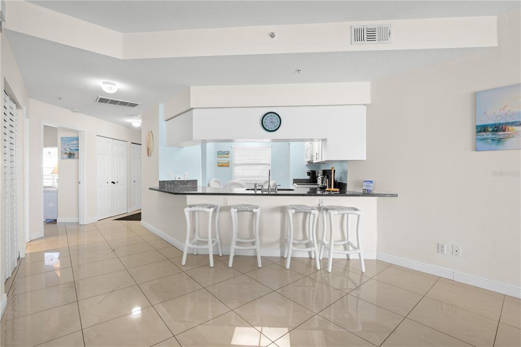 A kitchen with a breakfast bar, four white stools, and light-colored tile flooring — 12935 GULF LANE UNIT 205, MADEIRA BEACH, FL