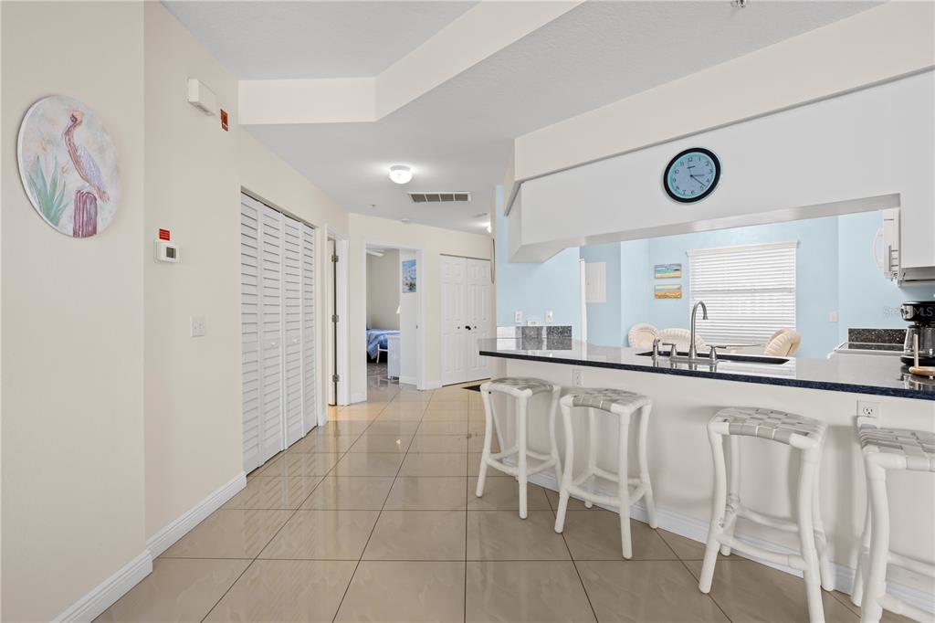 A kitchen with a breakfast bar, white stools, and tile flooring opens to a hallway — 12935 GULF LANE UNIT 205, MADEIRA BEACH, FL