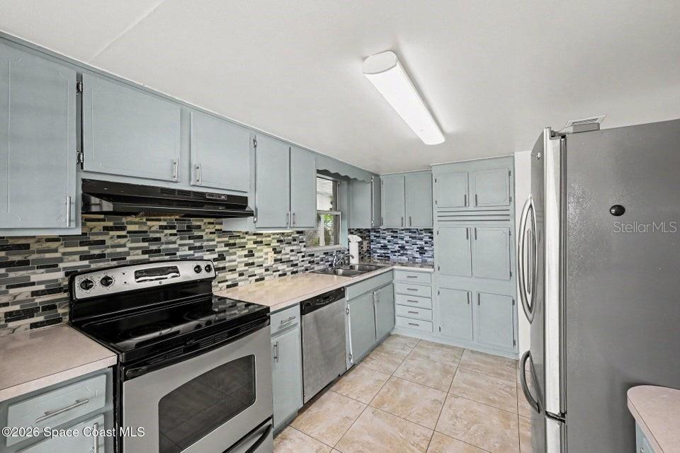 A kitchen features light blue cabinets, a patterned tile backsplash, and stainless steel appliances — 2292 LAKEVIEW DRIVE, MELBOURNE, FL