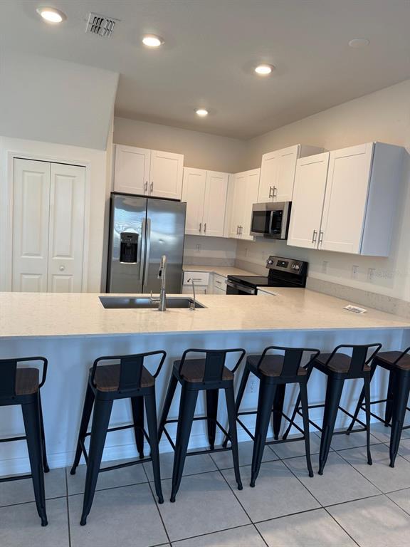 A kitchen features white cabinets, stainless steel appliances, a quartz island, and five bar stools — 10308 LAVENDER ASTER TRAIL, SAN ANTONIO, FL