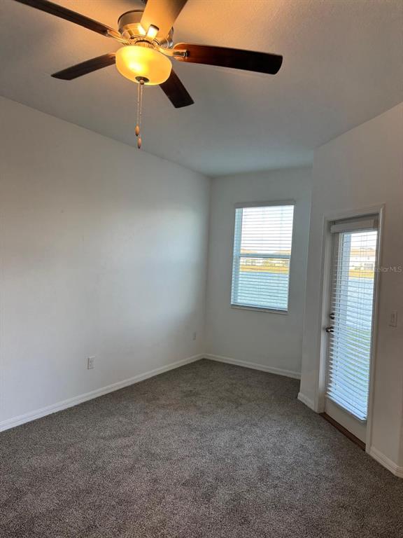 An empty room with gray carpet, white walls, a ceiling fan, a window, and a door — 10308 LAVENDER ASTER TRAIL, SAN ANTONIO, FL