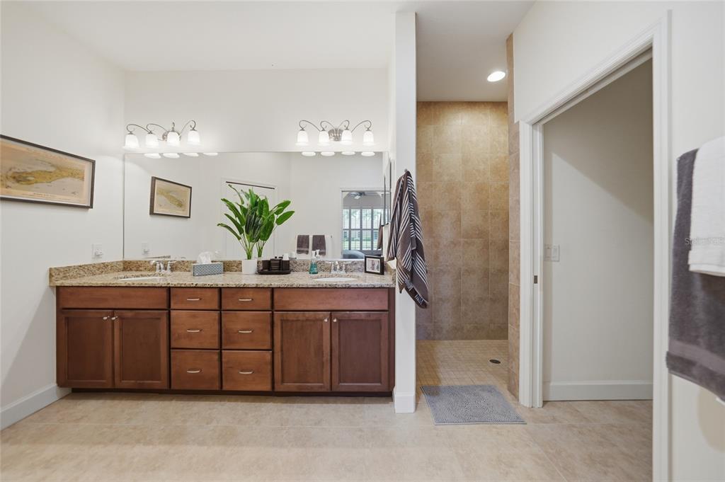 A bathroom features a double-sink vanity with wood cabinets, granite countertops, and a walk-in shower — 4691 TURNBERRY CIRCLE, NORTH PORT, FL