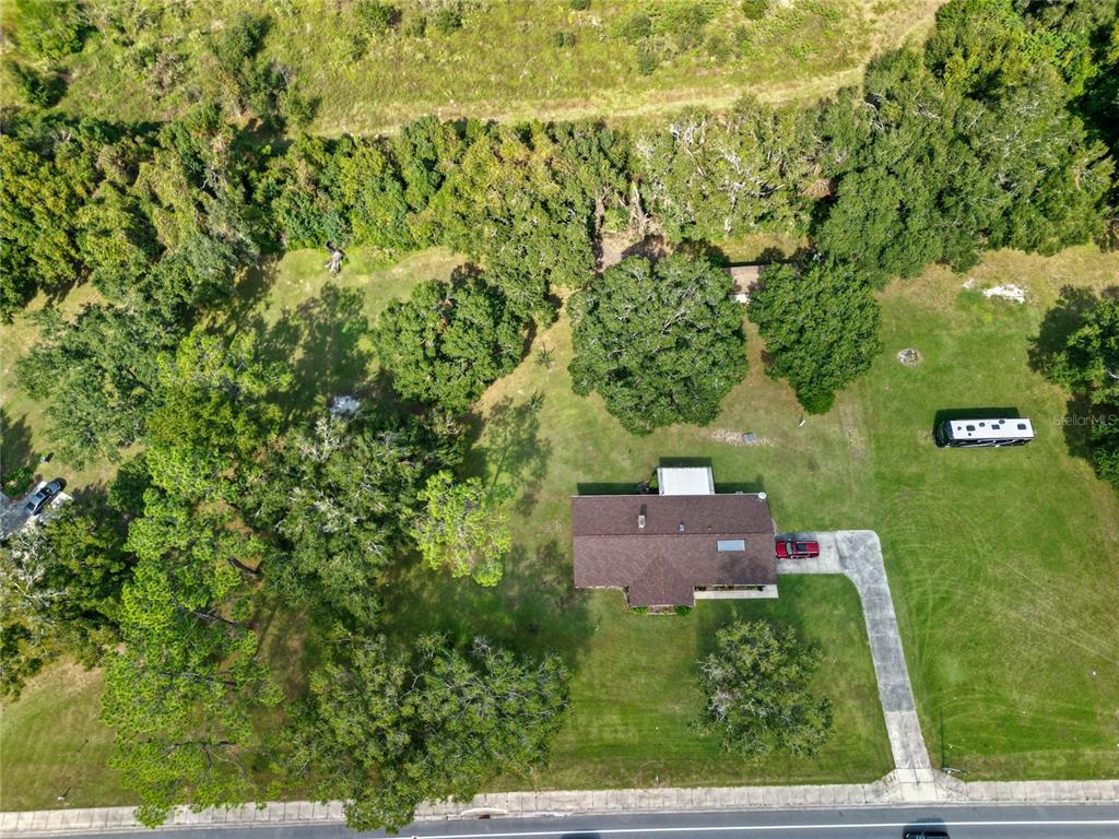 An aerial view shows a house with a brown roof, a driveway, and surrounding trees — 3696 E C-466, OXFORD, FL
