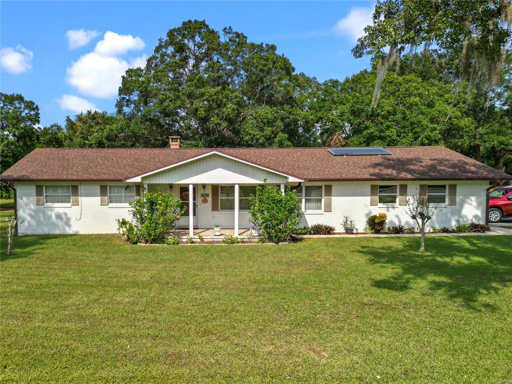 A single-story white house with a brown shingled roof and a front porch — 3696 E C-466, OXFORD, FL