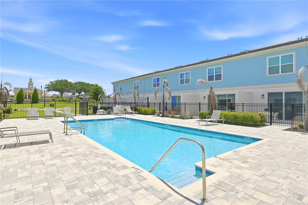 A rectangular swimming pool with a metal handrail sits on a paved patio beside townhomes — 7909 DRAW STREET, REUNION, FL