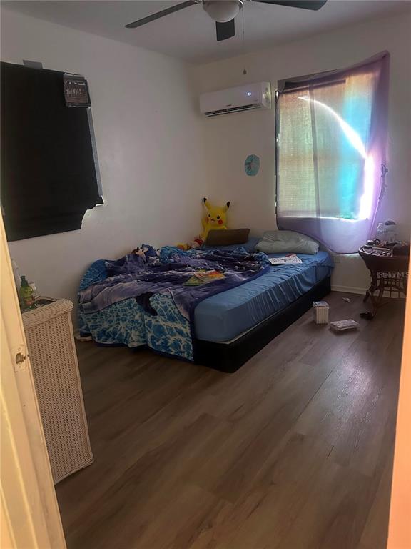 A bedroom features wood-look flooring, a bed with blue bedding, and a wall-mounted air conditioner — 1838 SW HARLEM CIRCLE, ARCADIA, FL