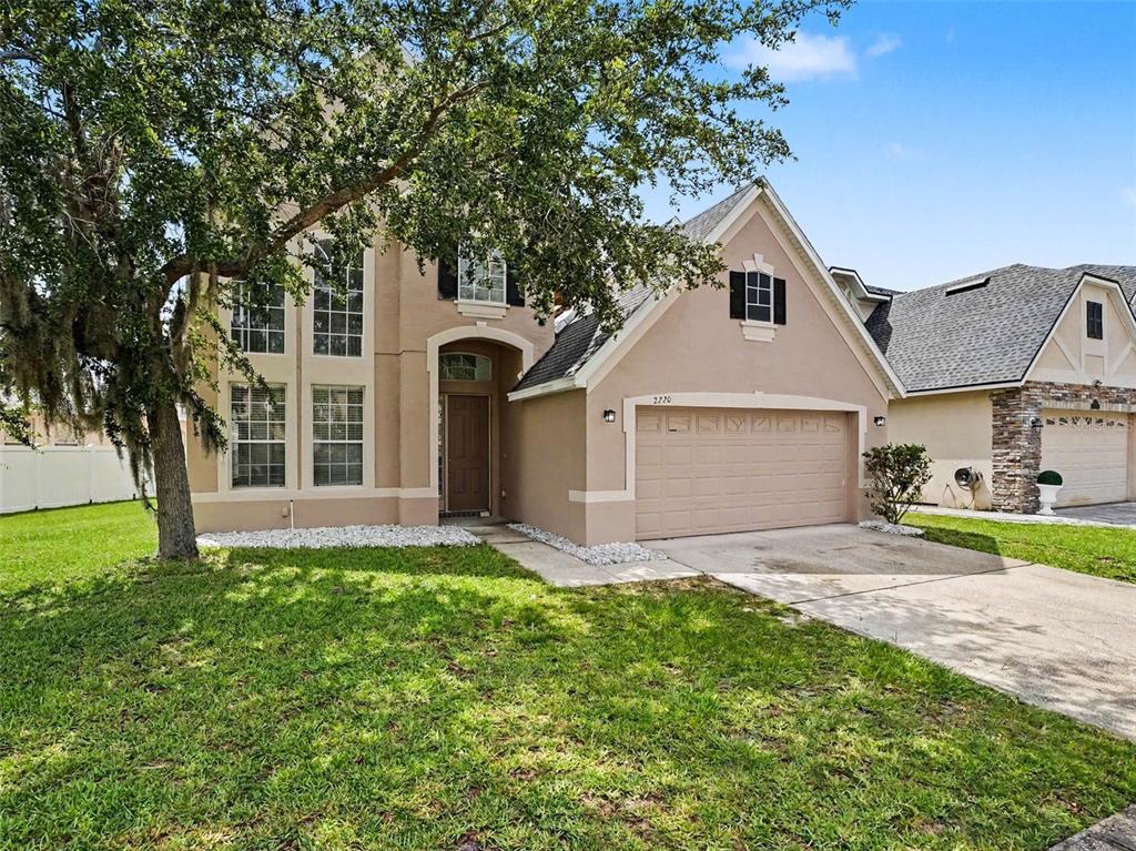 A two-story tan stucco house features a front-facing garage and a large oak tree — 2220 SAND ARBOR CIRCLE, ORLANDO, FL