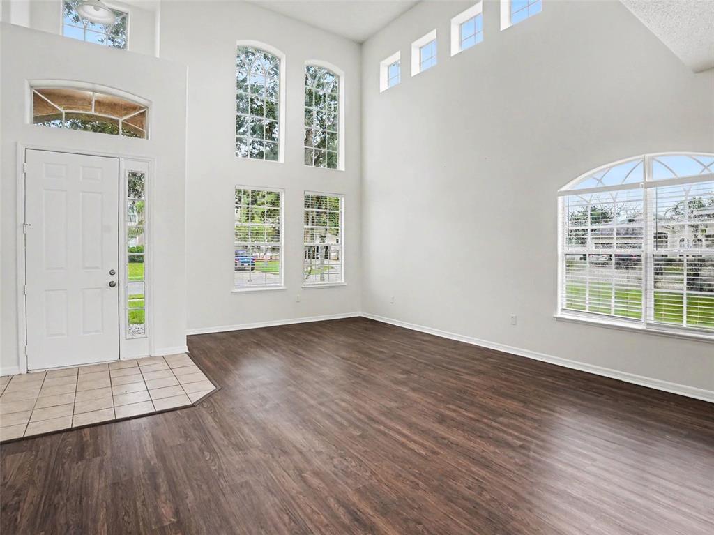 A bright, high-ceilinged living room features dark wood-look flooring, white walls, and multiple windows — 2220 SAND ARBOR CIRCLE, ORLANDO, FL