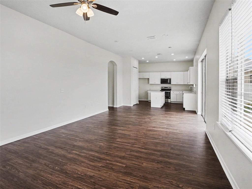An open-concept living area with dark wood-look flooring leads to a white kitchen — 2220 SAND ARBOR CIRCLE, ORLANDO, FL
