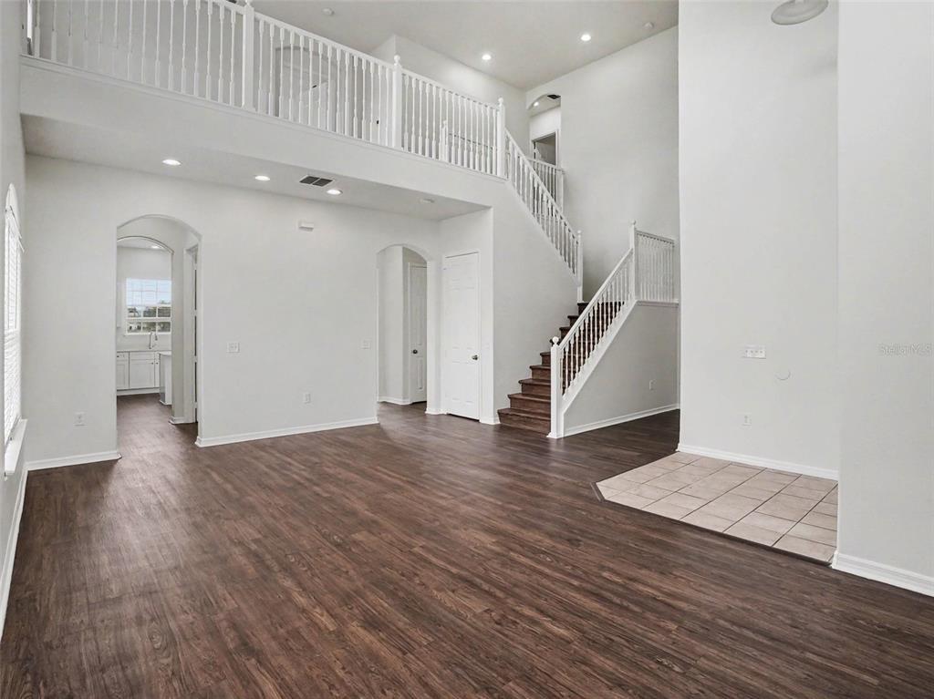 A spacious living area with dark wood floors, a staircase, and a second-floor balcony railing — 2220 SAND ARBOR CIRCLE, ORLANDO, FL