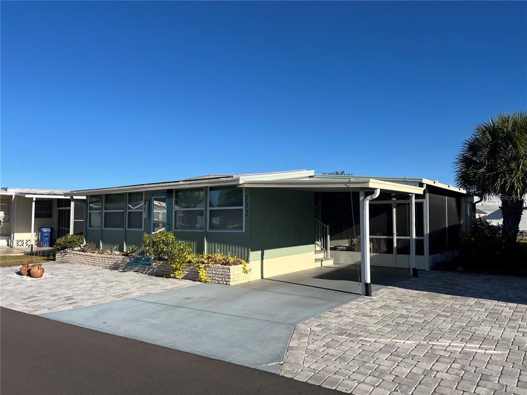 A single-story mobile home features a paved driveway, a carport, and a screened-in porch — 712 ROMA ROAD, VENICE, FL