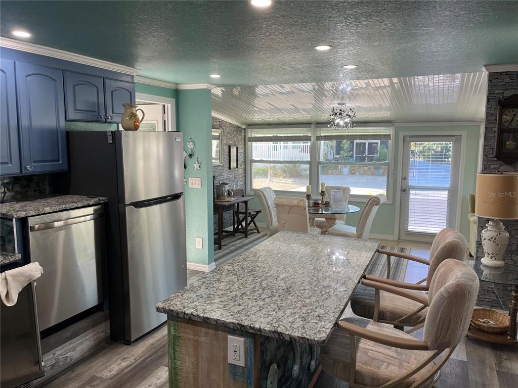 A kitchen features blue cabinets, a granite island, stainless steel appliances, and a dining area — 712 ROMA ROAD, VENICE, FL
