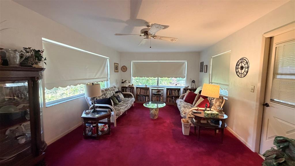 A living room features red carpeting, two sofas, bookshelves, and a ceiling fan — 212 S LUCILLE STREET, BEVERLY HILLS, FL