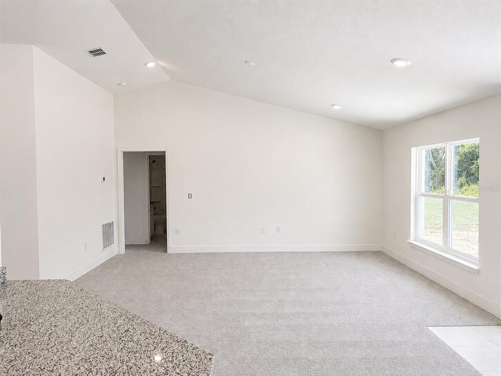 An empty room with vaulted ceilings, gray carpet, and a doorway leading to a bathroom — 1680 ANN ROSE WAY, LEESBURG, FL