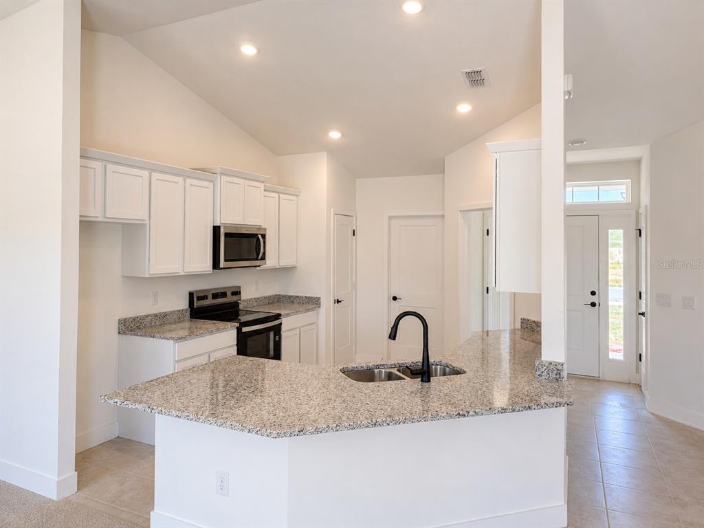 A kitchen features white cabinets, granite countertops, a stainless steel stove, and a black faucet — 1680 ANN ROSE WAY, LEESBURG, FL