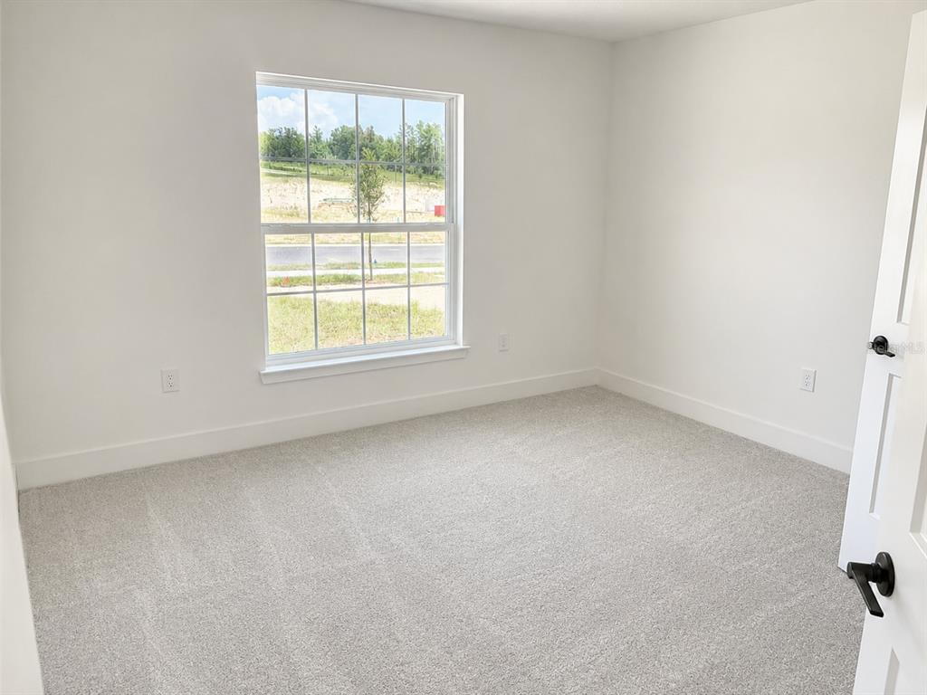 An empty bedroom features white walls, light gray carpeting, and a window with exterior views — 1680 ANN ROSE WAY, LEESBURG, FL