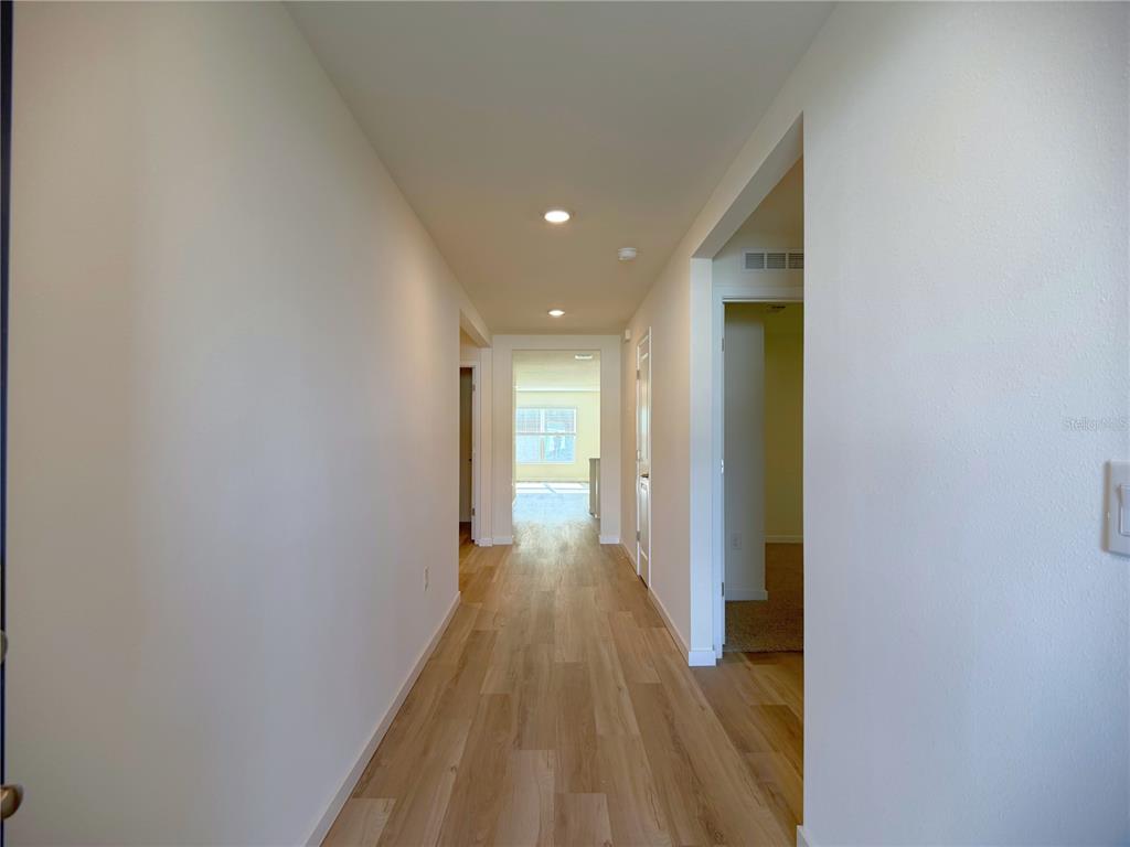 A hallway with light wood-look flooring leads toward a bright room with a window — 7230 SE 112TH LANE, BELLEVIEW, FL