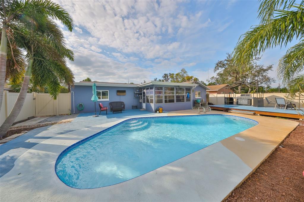 A backyard features a swimming pool, a blue-painted house, and a wooden deck with a grill — 12341 79TH PLACE, SEMINOLE, FL