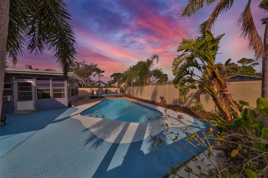A backyard features a swimming pool, blue patio, palm trees, and a wooden deck at sunset — 12341 79TH PLACE, SEMINOLE, FL