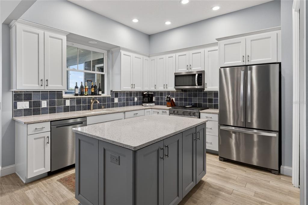 A kitchen with white cabinets, a gray island, stainless steel appliances, and dark tiled backsplash — 260 S CENTRAL AVENUE, UMATILLA, FL