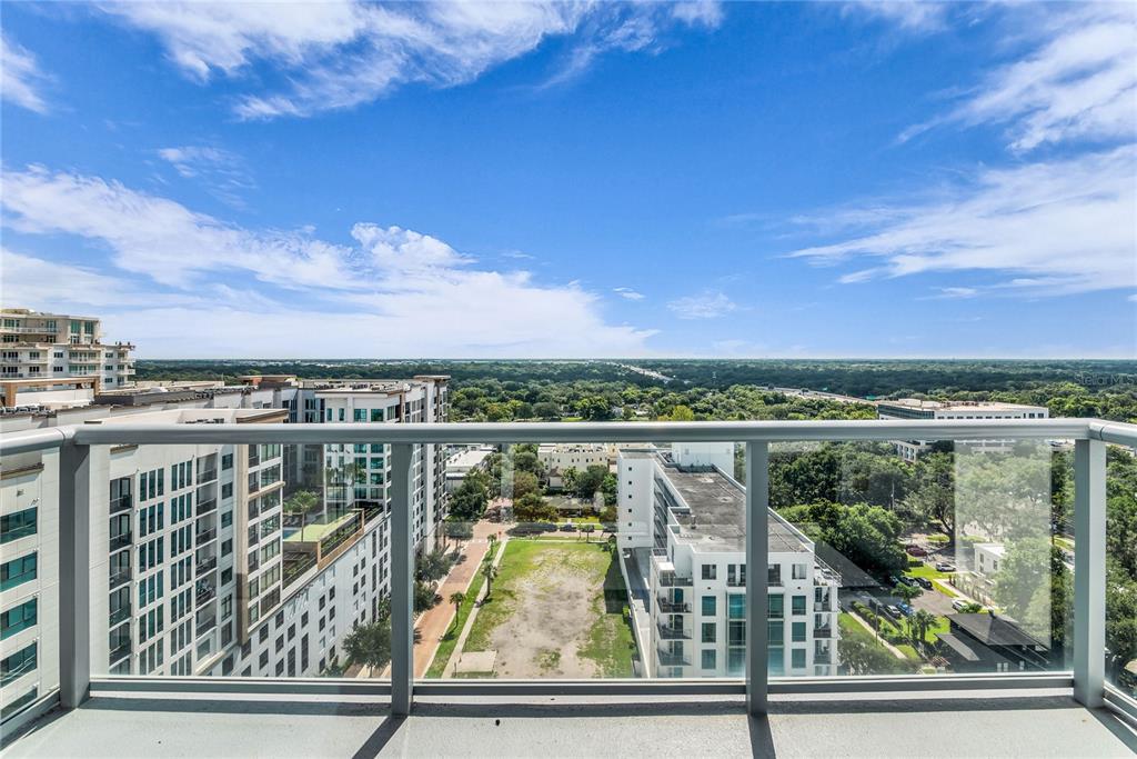 A high-rise balcony overlooks a city street, surrounding apartment buildings, and a distant green landscape — 260 S OSCEOLA AVENUE UNIT 1602, ORLANDO, FL